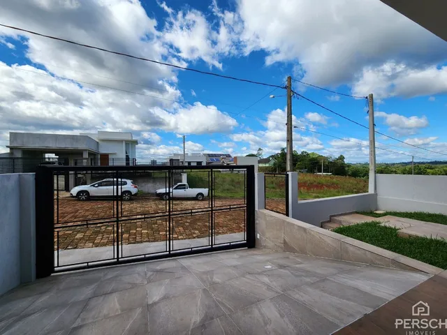 Foto da entrada de uma propriedade com portão e área pavimentada.