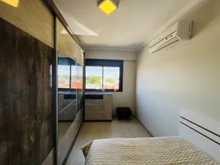 Quarto com armário em madeira e vista pela janela.