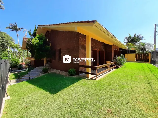 Fachada de casa de tijolos vermelhos com jardim gramado e deck de madeira.