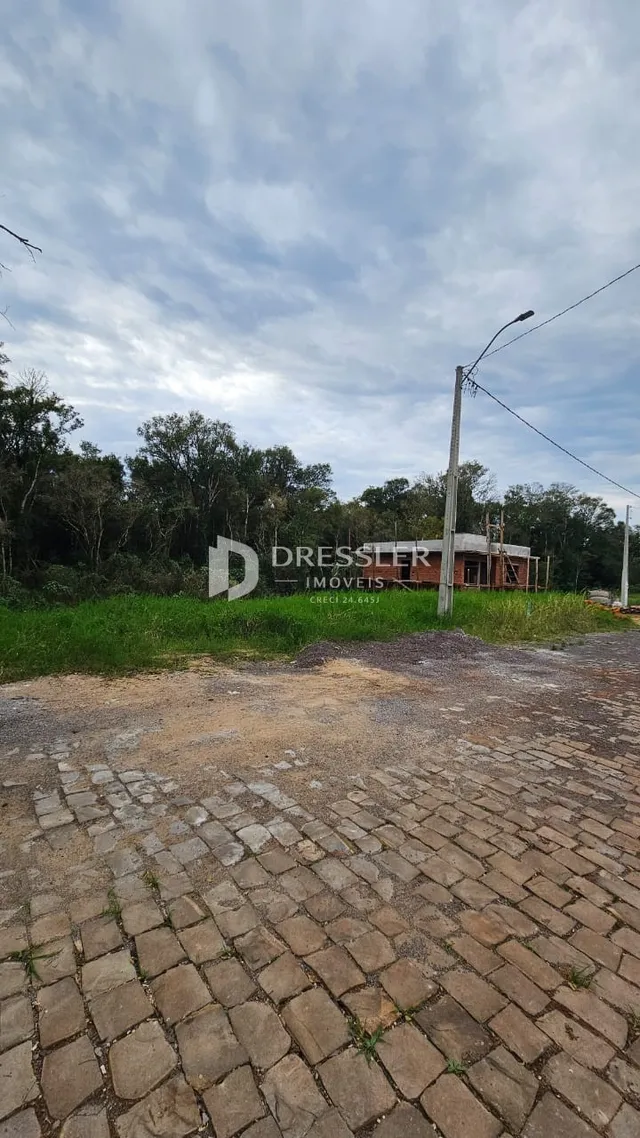 Vista externa de uma propriedade com pavimentação de paralelepípedos e vegetação ao fundo.