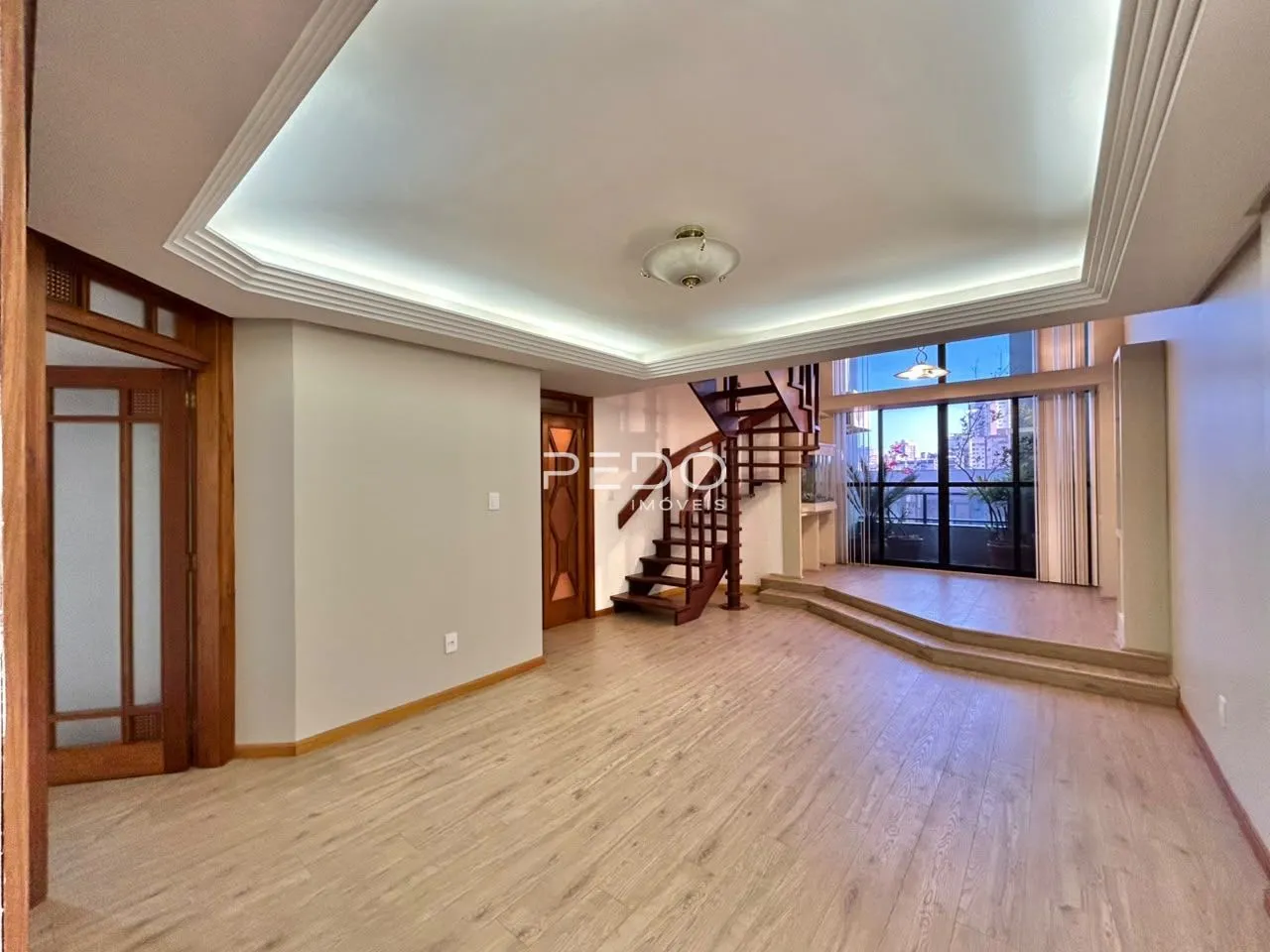 Sala de estar com piso de madeira clara e escadaria visível.