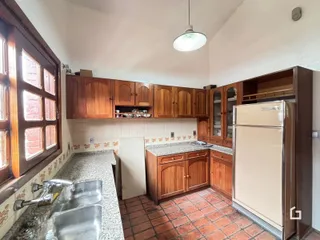 Vista da cozinha com armários de madeira e piso de tijolos.