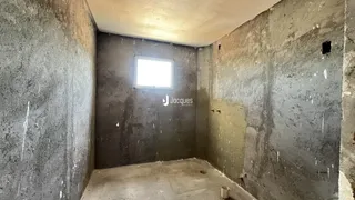 Uma foto de um cômodo interno com paredes de concreto cru e uma janela.