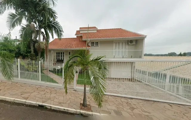 Exterior da casa residencial em Lajeado, Brasil, com muro branco e paisagismo.