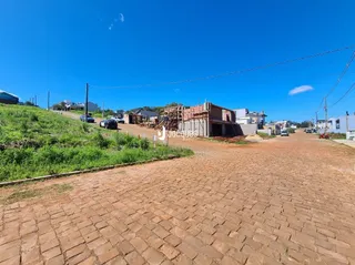 Vista externa de uma propriedade com terreno inclinado e área pavimentada.
