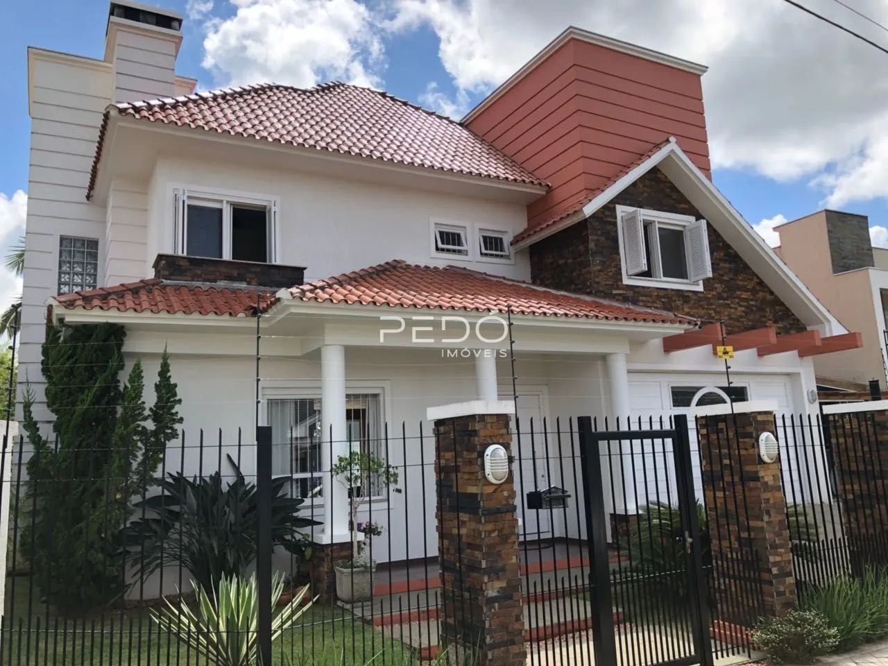 Fachada de uma residência em Lajeado, Brasil, com telhado de telhas vermelhas e cerca de ferro preta.