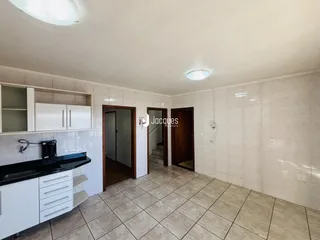 Vista interna de uma cozinha com armários brancos e piso de cerâmica.