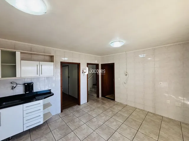 Vista interna de uma cozinha com armários brancos e piso de cerâmica.