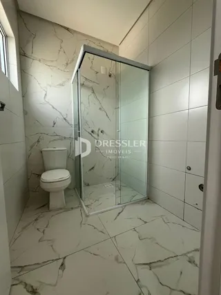 Banheiro com revestimento em mármore branco e box de vidro.