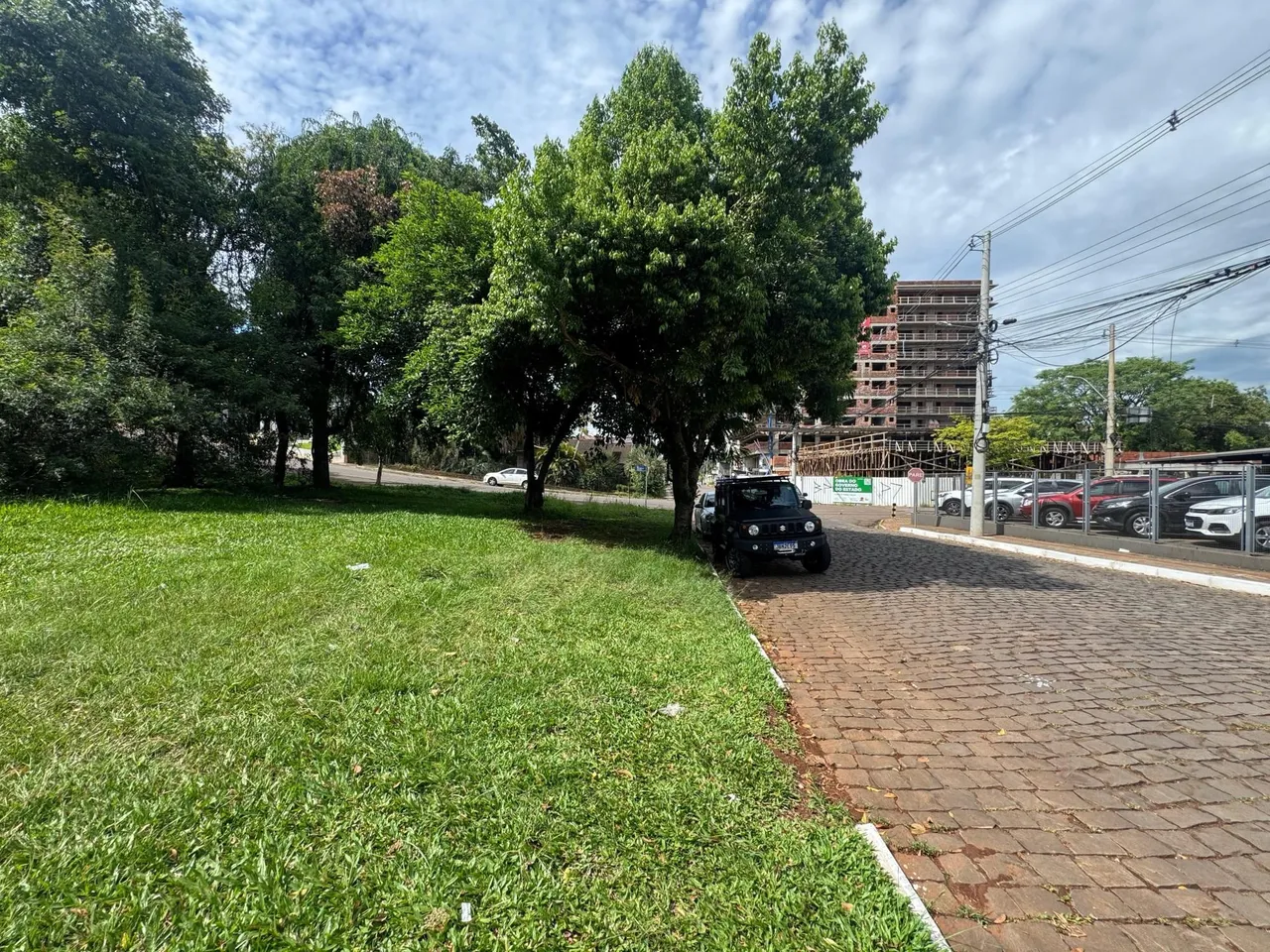 Vista externa de um terreno com gramado verde e árvores sob um céu nublado.