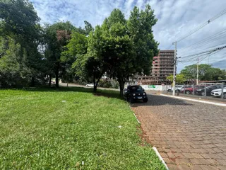 Vista externa de um terreno com gramado verde e árvores sob um céu nublado.