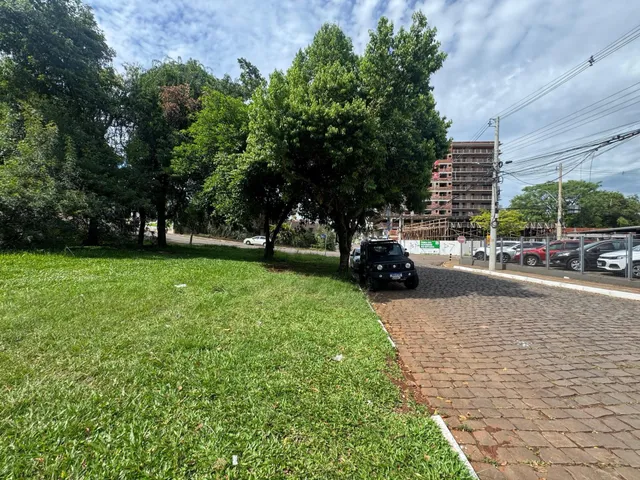 Vista externa de um terreno com gramado verde e árvores sob um céu nublado.