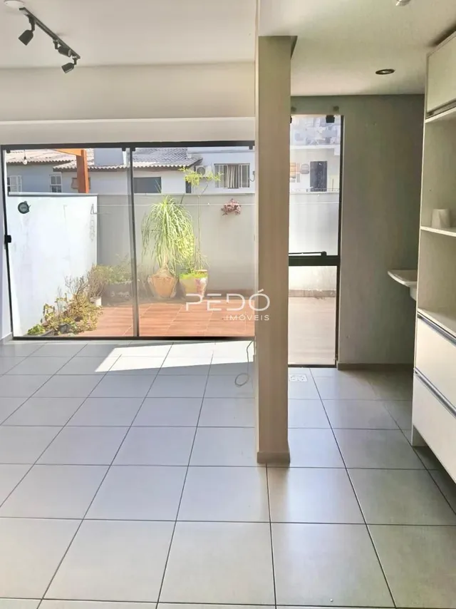 Vista interna de uma área com piso de cerâmica e portas de vidro que dão acesso ao exterior.