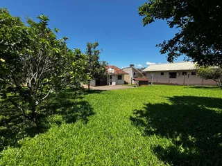 Vista externa da propriedade mostrando um gramado verde e árvores sob um céu azul.