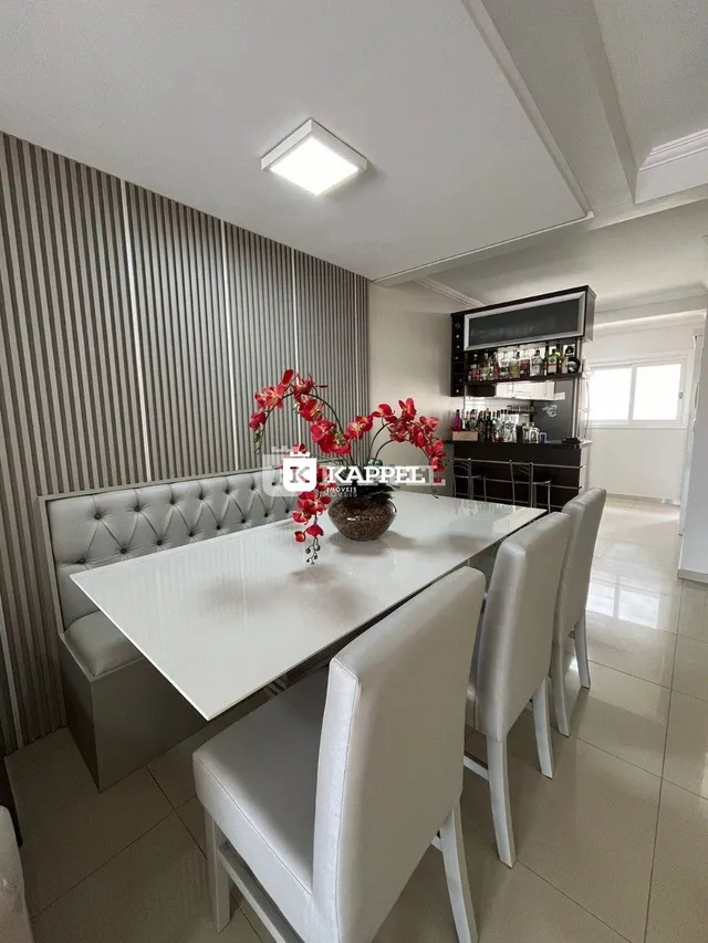 Imagem de um ambiente interno com mesa de jantar e cadeiras brancas.