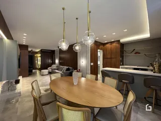 Vista da sala de jantar com mesa de madeira e luminárias pendentes.