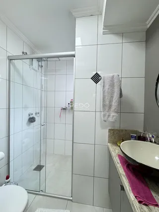Foto de um banheiro com box de vidro e revestimento cerâmico branco.