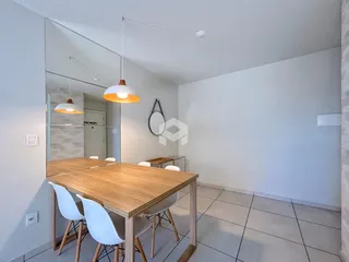 Foto de um ambiente interno com mesa de jantar de madeira e cadeiras brancas.
