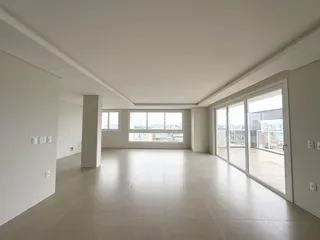 Ambiente interno de uma sala ampla com piso claro e grandes janelas.