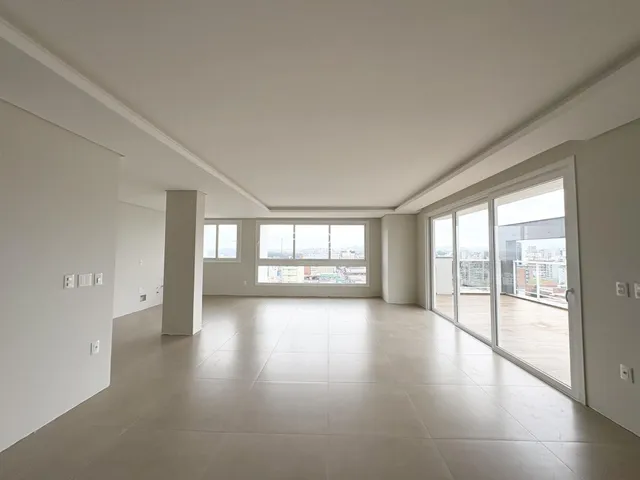 Ambiente interno de uma sala ampla com piso claro e grandes janelas.