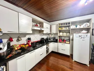 A cozinha apresenta armários brancos e bancadas escuras com piso de madeira.