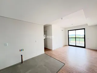 Ambiente interno de uma sala ampla com piso de madeira e vista para o exterior.