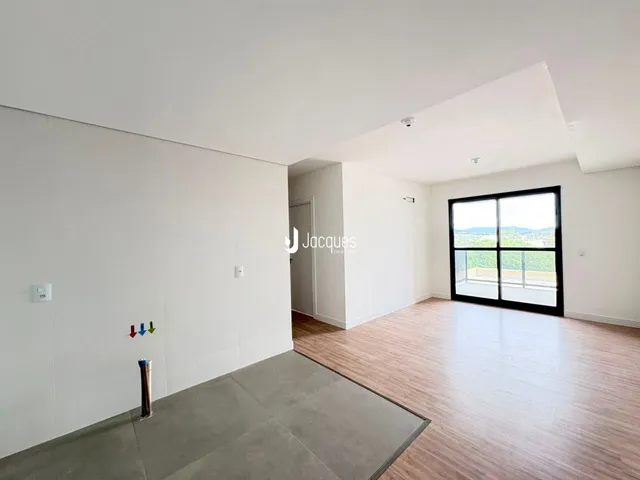 Ambiente interno de uma sala ampla com piso de madeira e vista para o exterior.