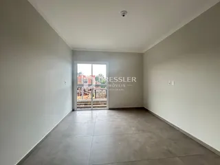 Interior de uma sala ampla com piso de cerâmica e parede branca.