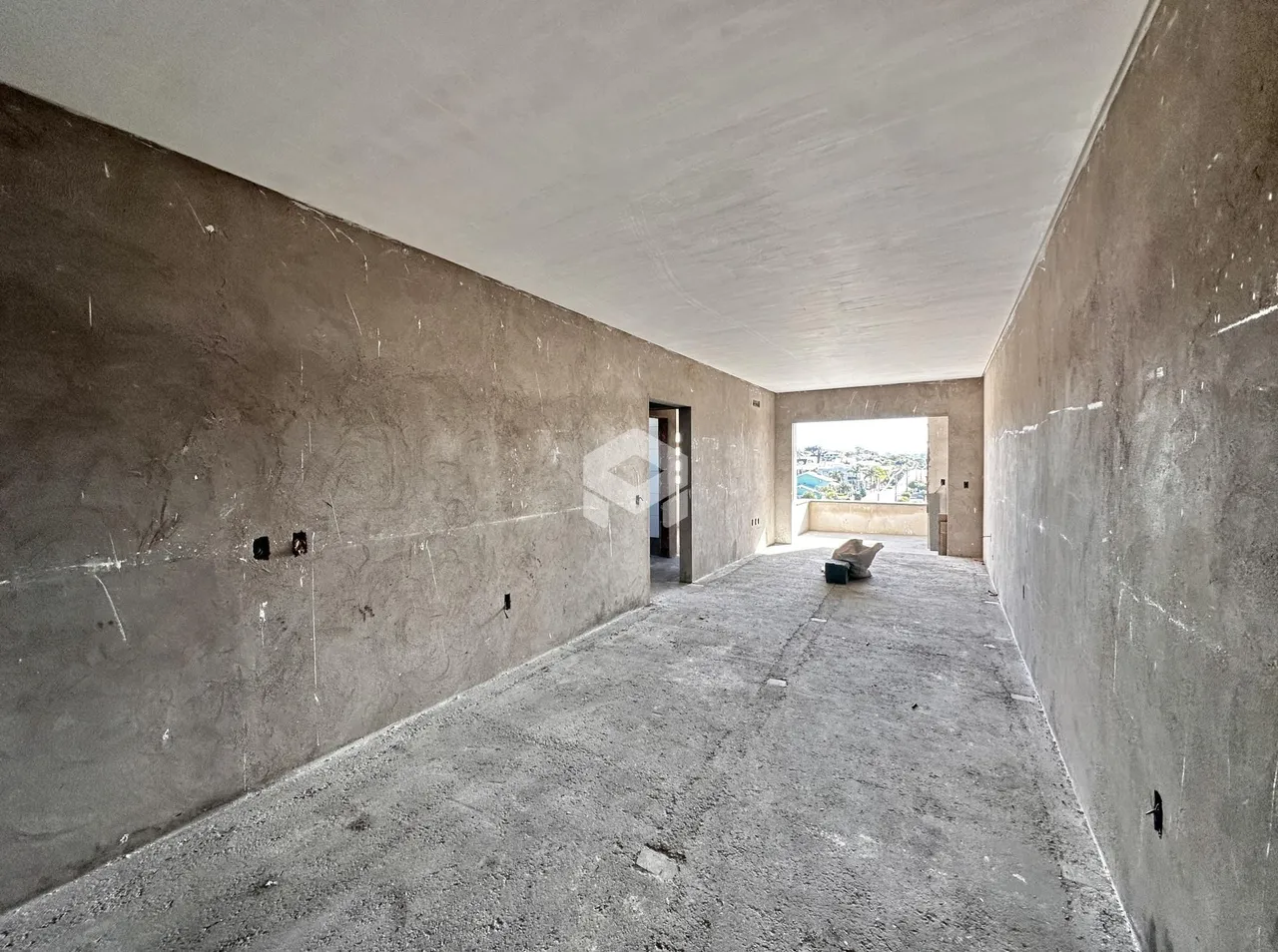 Corredor interno com paredes de concreto aparente e piso de concreto.