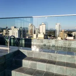 Varanda com piso de cerâmica e guarda-corpo de vidro com vista da cidade.