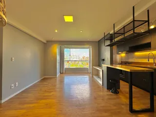 Sala de estar com piso de madeira e cozinha moderna em um apartamento.