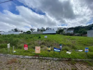 Foto da fachada de uma propriedade com grama alta e placas de venda no primeiro plano.