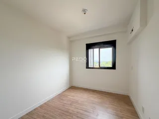 Vista interna de um cômodo com paredes brancas e piso de madeira clara.