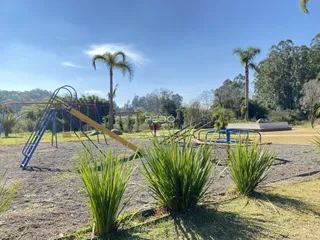 Uma vista externa de um jardim com equipamentos de playground e vegetação.