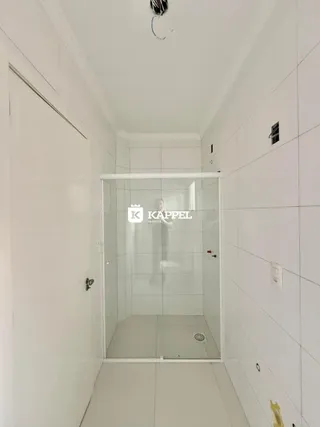 Corredor branco com um box de banheiro de vidro.