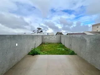 Vista externa de um quintal gramado cercado por um muro de concreto.