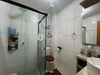 Banheiro com revestimento cerâmico e box de vidro.