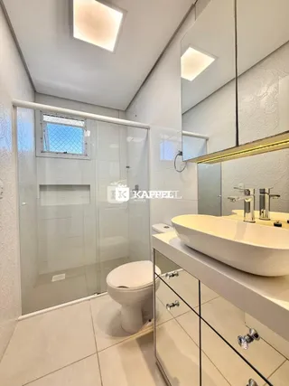 Banheiro moderno com box de vidro e pia branca.