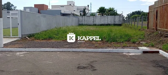 Foto da fachada de uma propriedade mostrando um muro de concreto e área externa com vegetação.