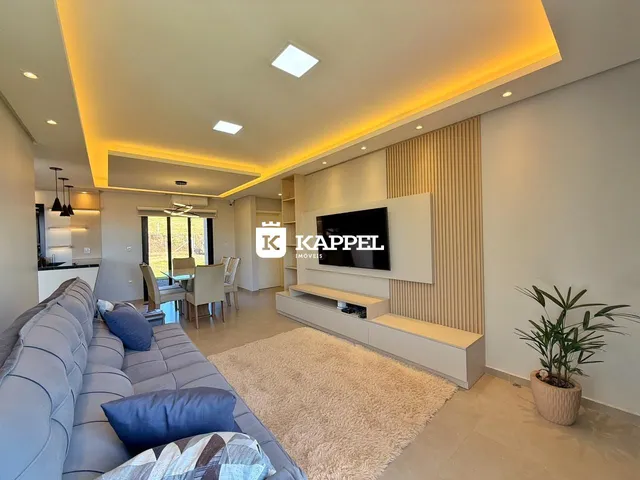 Sala de estar moderna com sofá grande e televisão em uma sala bem iluminada.