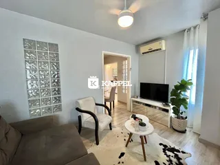 Sala de estar com sofá, poltrona e televisão em ambiente claro.