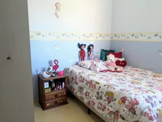 Quarto com cama decorada e um móvel de madeira ao lado.
