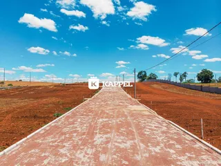 Vista de uma estrada rural em uma área de terra vermelha sob um céu azul com nuvens.