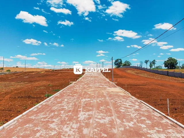 Vista de uma estrada rural em uma área de terra vermelha sob um céu azul com nuvens.