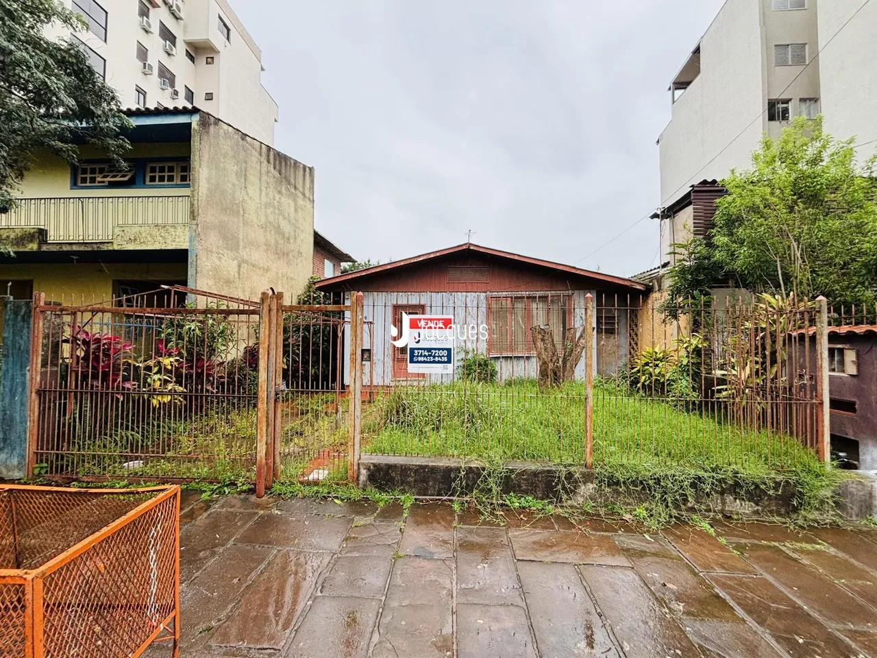 Vista externa de uma propriedade com cerca de metal e vegetação alta.