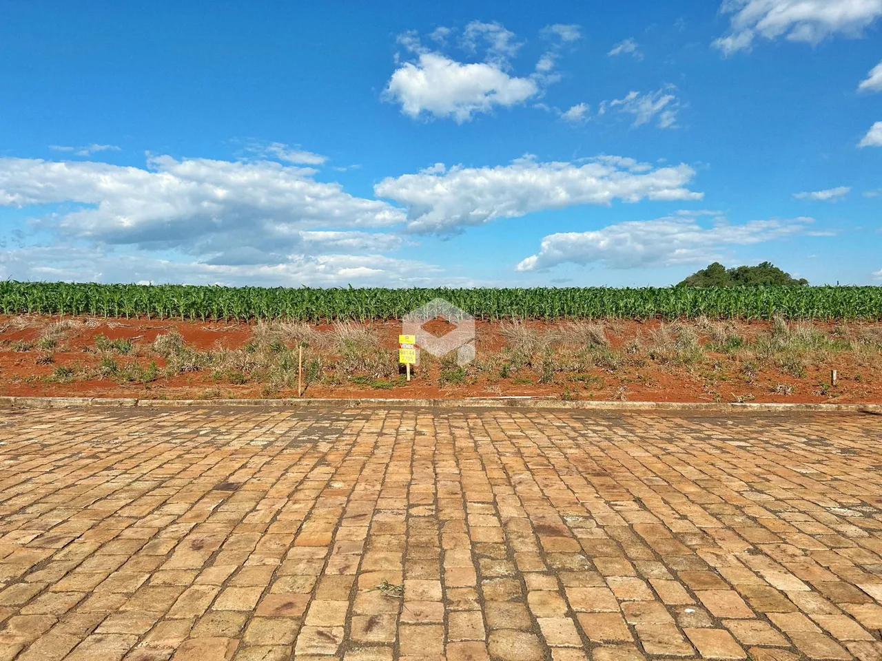 Vista da propriedade com área pavimentada e campo de cultivo ao fundo.