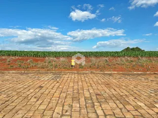 Vista da propriedade com área pavimentada e campo de cultivo ao fundo.