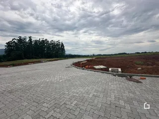 Vista externa de uma área pavimentada com terra e vegetação ao fundo.