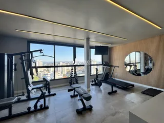 Imagem de um espaço interno com grandes janelas e equipamentos de ginástica.