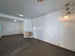 Uma sala ampla com piso de madeira escura e paredes brancas.